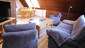 A cozy living room with a flat-screen TV, a wooden dining table, and two sofas. - Ferienwohnung in Westerland (Sylt)