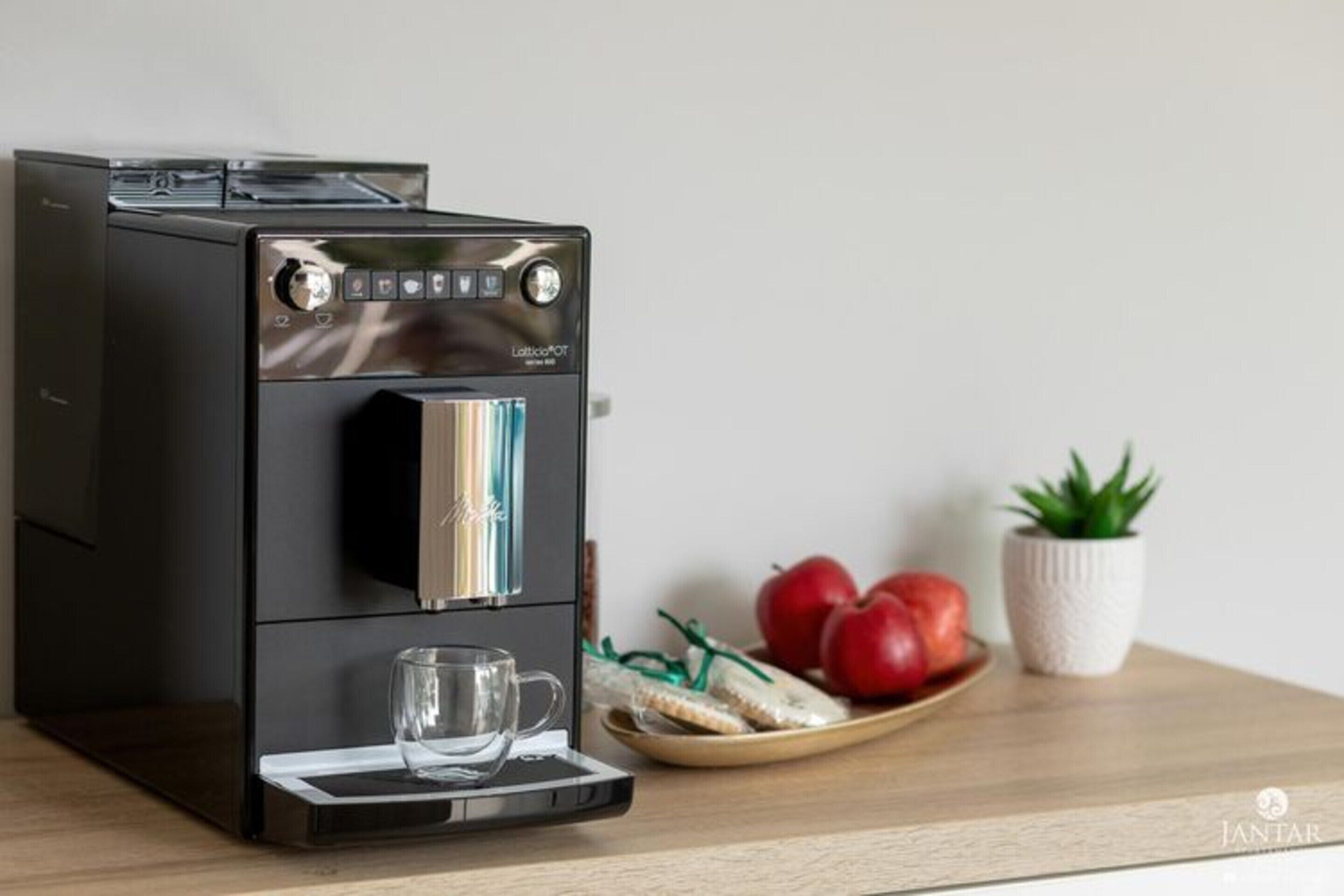 Una macchina da caffè con serbatoio dell'acqua, portabicchieri in vetro e un piatto con mele e pane.