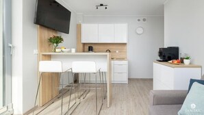 Egy modern konyha, melyben síkképernyős televízió, fehér szekrények és egy bársarok található, bárszékekkel.