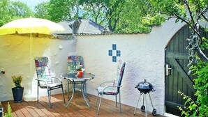 Une terrasse extérieure avec un parasol jaune, deux chaises en métal, une petite table et un barbecue.