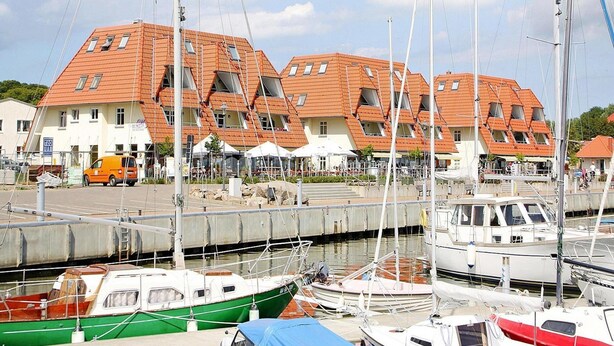 Un port de plaisance avec des bateaux amarrés, une rangée de bâtiments aux toits inclinés et un ciel dégagé.