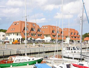 A marina with boats docked, a row of buildings with sloped roofs, and a clear sky. - Ferienhaus in Wiek (Wiek)