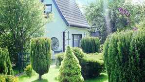 Une maison à deux étages, dotée d’un toit à forte pente, entourée de haies et d’arbres bien entretenus.