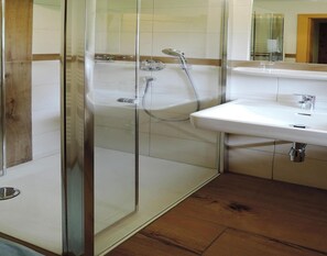 Une salle de bain avec une douche à parois de verre, un lavabo blanc et un plancher en bois.