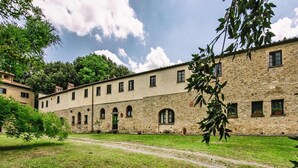 A courtyard with a stone building featuring arched windows and doorways, surrounded by greenery. - Country House in Tuscany With Pool and Olive Grove (Capannoli)