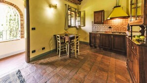 A rustic kitchen with a tiled backsplash, wooden cabinets, and a dining area with a table and chairs. - Country House in Tuscany With Pool and Olive Grove (Capannoli)