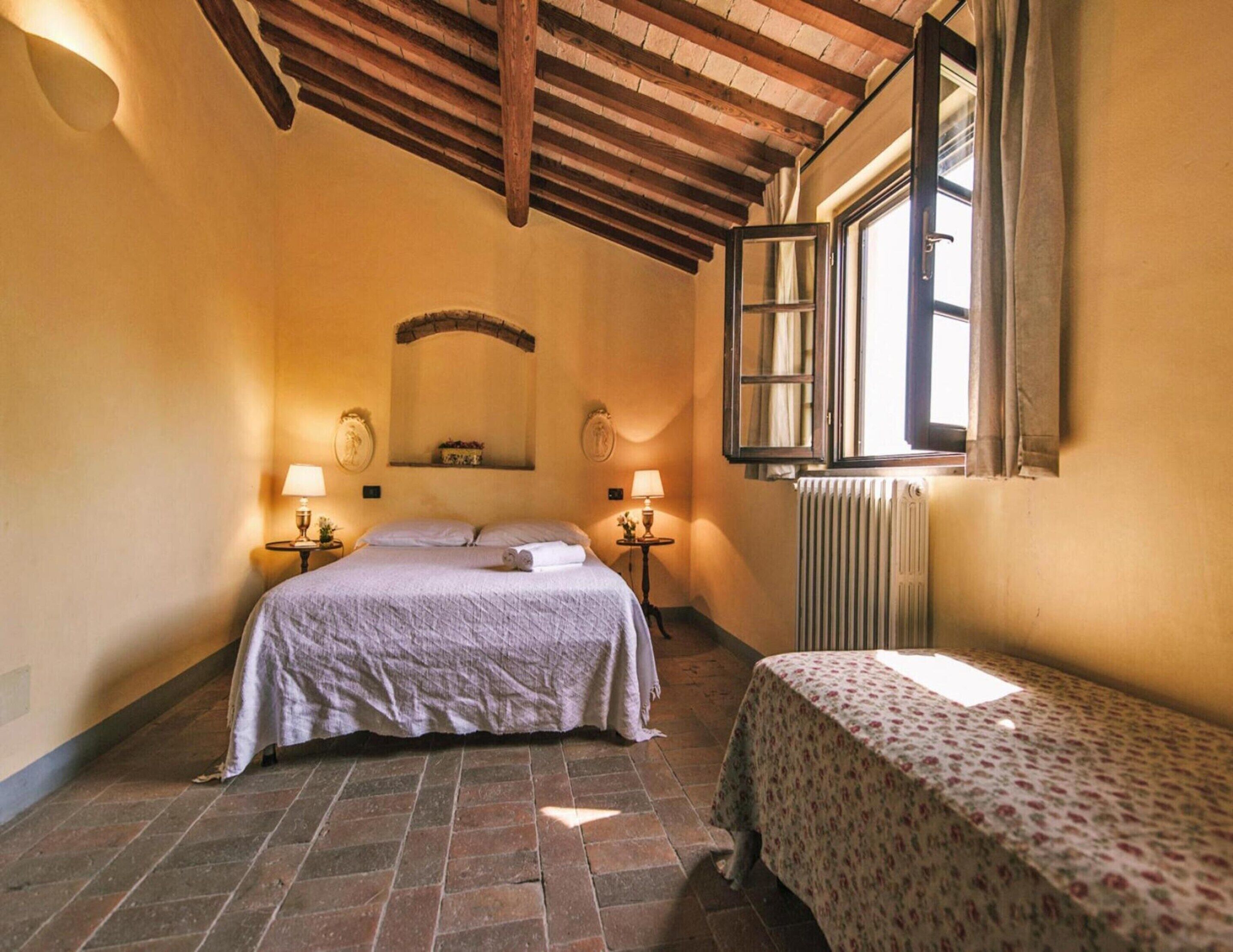 Een slaapkamer met een bed, een klein tafeltje, een radiator en een raam met gordijnen.