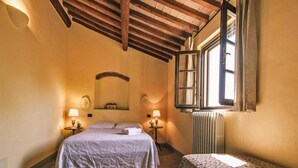 A bedroom with a bed, a small table, a radiator, and a window with curtains. - Country House in Tuscany With Pool and Olive Grove (Capannoli)