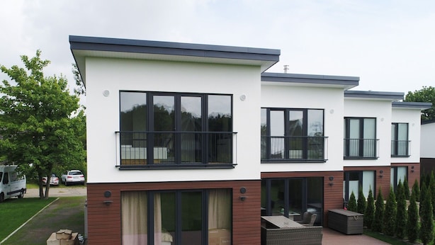 Un immeuble résidentiel moderne à deux étages, doté de grandes fenêtres, de balcons et d’un patio couvert.