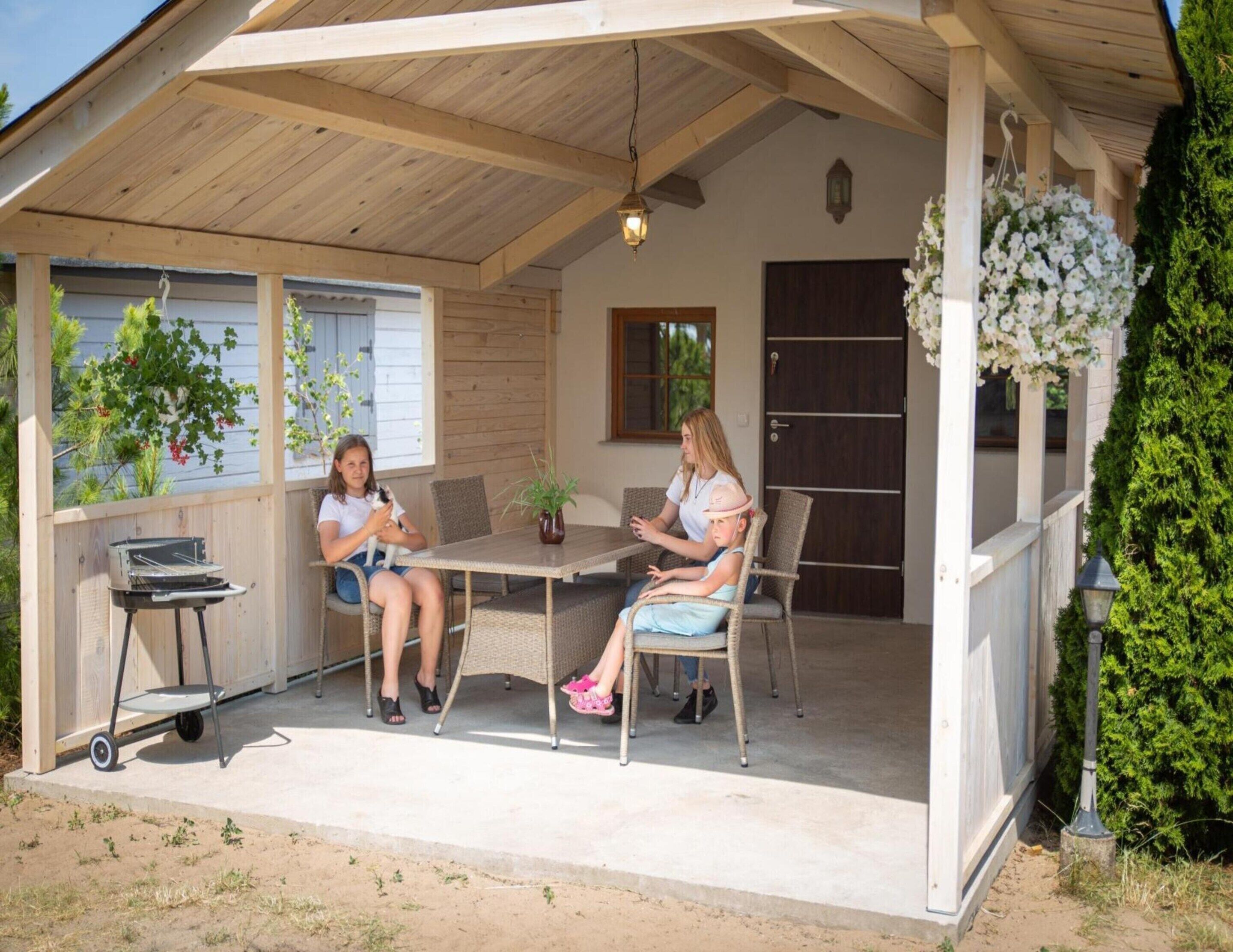 Ein überdachter Außenbereich mit Tisch und Stühlen, einem Grill und Topfpflanzen.