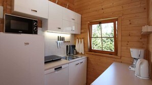 A compact kitchen with white cabinets, a microwave, a coffee maker, and a window with a view of greenery. - Bungalow in Miedzyzdroje With a Terrace (Miedzyzdroje)
