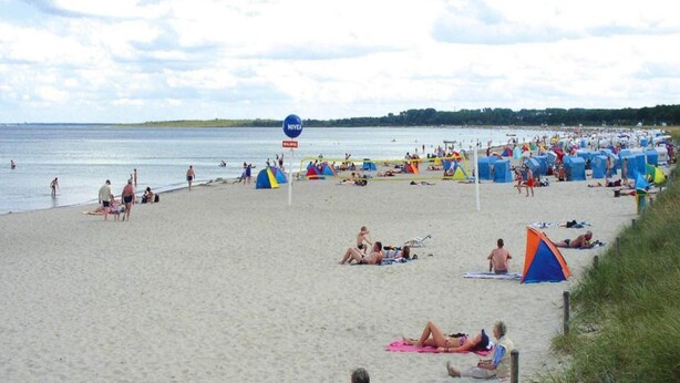 Ein voller Strand mit Zelten und sonnenbadenden Menschen.
