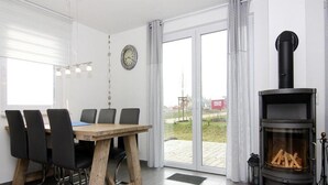 Ein Essbereich mit Holztisch und -stühlen, einem schwarzen Herd mit Holzvorrat und Blick durch große Glastüren.