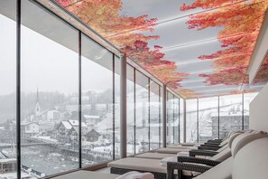 Un intérieur moderne avec de grandes fenêtres, un coin salon et une vue sur une ville enneigée.