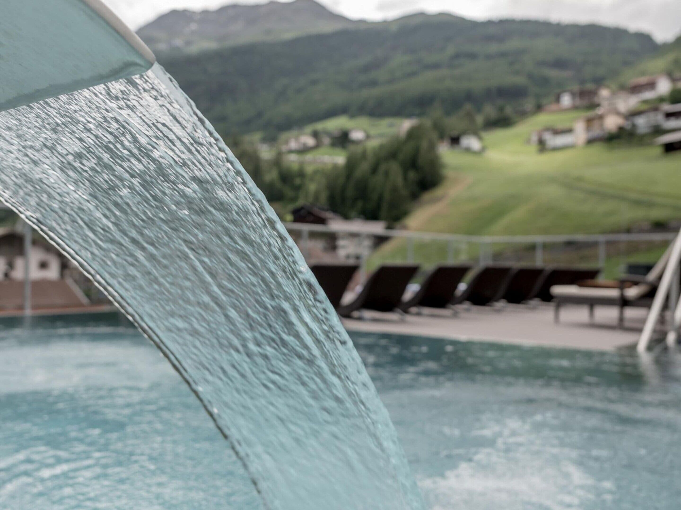 Ein Pool mit Wasserfällen, umgeben von einer malerischen Hügellandschaft und einer Reihe von Häusern.