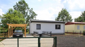 Un piccolo edificio con un'auto parcheggiata sotto un portico di legno, circondato da un'area recintata e alberi.