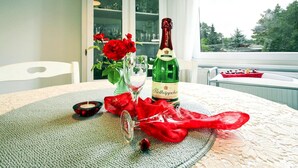 Un tavolo con una bottiglia di Rölkäppchen, un bicchiere, rose rosse e un tessuto rosso.
