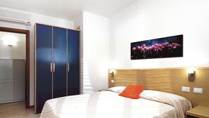 Habitación de hotel con cama, mesita de noche, cabecera de madera, un cuadro colgado en la pared y un armario.