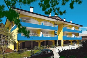 Un immeuble de deux étages doté de balcons, une voiture garée devant, et un ciel bleu dégagé.
