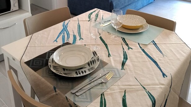 Un coin repas avec une table dressée pour deux personnes, un canapé bleu en arrière-plan et un luminaire fixé au mur.