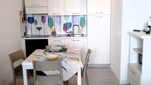 Une cuisine compacte avec des meubles blancs, une table à manger avec des chaises et un petit îlot central doté d’un micro-ondes.