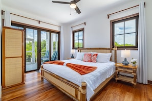 A bedroom with a bed, a ceiling fan, a nightstand with a lamp, and a view through the window.