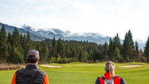 A golf course with a mountainous backdrop, a flagstick, and players with golf bags. - Chalet Rabl, Westendorf (Westendorf)