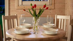 Une table à manger en bois, avec de l’assiette blanche et des verres à vin vides, un vase rempli de tulipes rouges et une fenêtre donnant sur des immeubles.