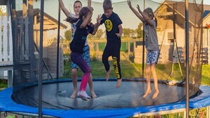 Un trampoline doté d’un filet de sécurité, entouré d’une clôture en bois et d’une petite clôture blanche.