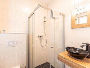 Un baño moderno con ducha acristalada, tocador de madera y un lavabo oscuro, además de un espejo sobre el lavabo.