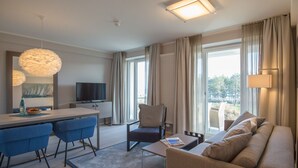 Una habitación de hotel moderna con comedor, sofá, televisor y ventanas amplias.