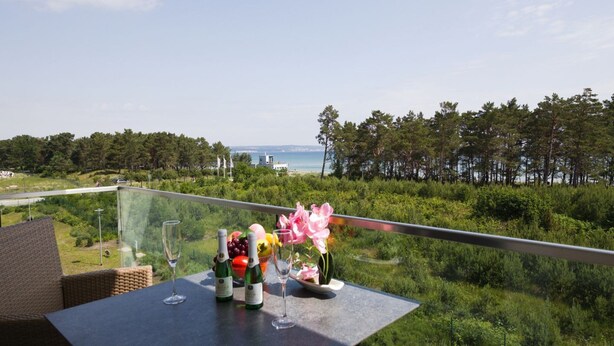 Un balcón con una mesa lista para comer, con vistas a un paisaje costero con árboles y el mar.