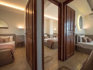 A hotel room with a large bed, a smaller bed, a sofa, and a desk. There are two doors leading to other rooms.