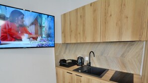 Una cocina moderna con armarios de madera, un lavamanos negro y un televisor en la pared mostrando un programa.