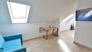 Una habitación moderna con un sofá azul, una mesa de comedor con sillas, un televisor montado en la pared y un tragaluz.