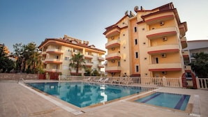 A hotel with a swimming pool, multiple balconies, and a clear sky. - Sevgi Tatil Sitesi (Alanya)