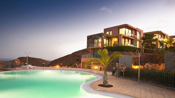 Ein modernes Hotel mit Schwimmbad, einer Palme und Blick auf die Hügel.