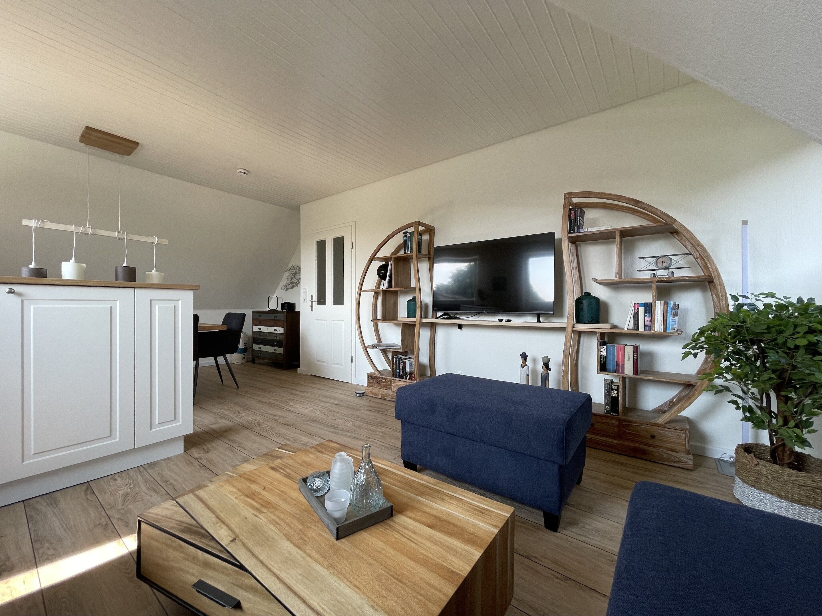 A modern living room with a flat-screen TV, wooden shelving, a blue sofa, and a coffee table.