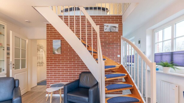 Un interior moderno con una pared de ladrillo, una escalera de madera con peldaños cubiertos de moqueta azul, un sillón de cuero negro y una pequeña mesa.