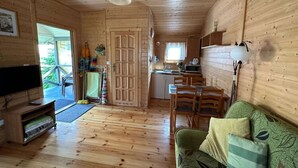 L’intérieur d’un chalet en bois comprend un téléviseur, un canapé, une table à manger et un coin cuisine.