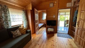 L’intérieur d’un chalet en bois, avec un canapé, un téléviseur et une porte donnant sur un espace extérieur.