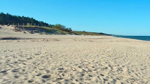 Une vaste plage de sable fin, à pente douce, sous un ciel bleu et dégagé.