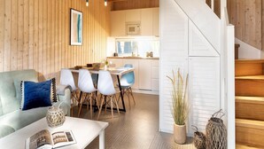 Ein gemütliches Wohnzimmer mit Sofa, Esstisch und Stühlen, verbunden mit einer Küche und einer weißen Treppe.