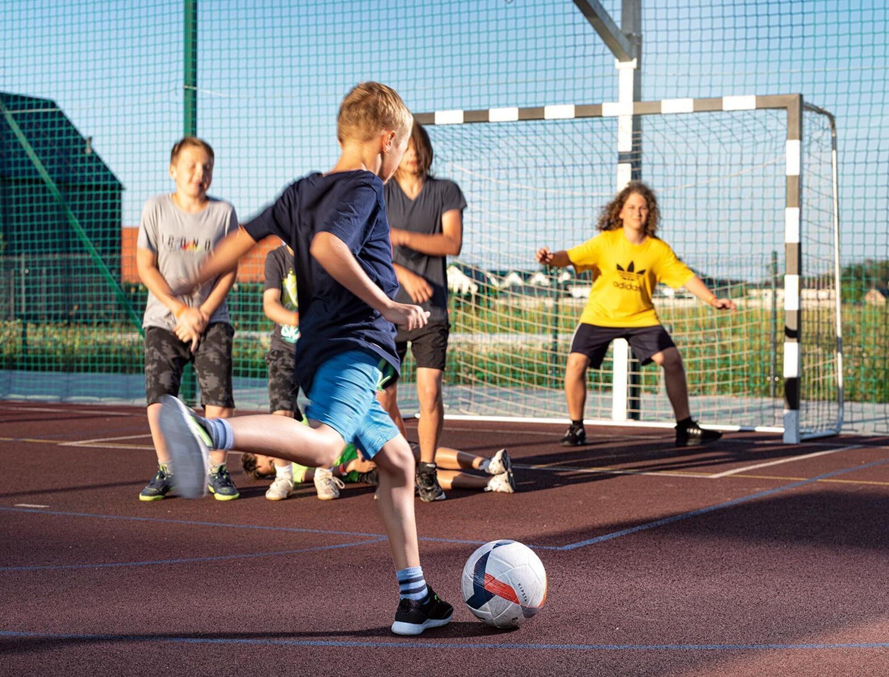 A group of people playing soccer on a track field with a goalpost in the background.