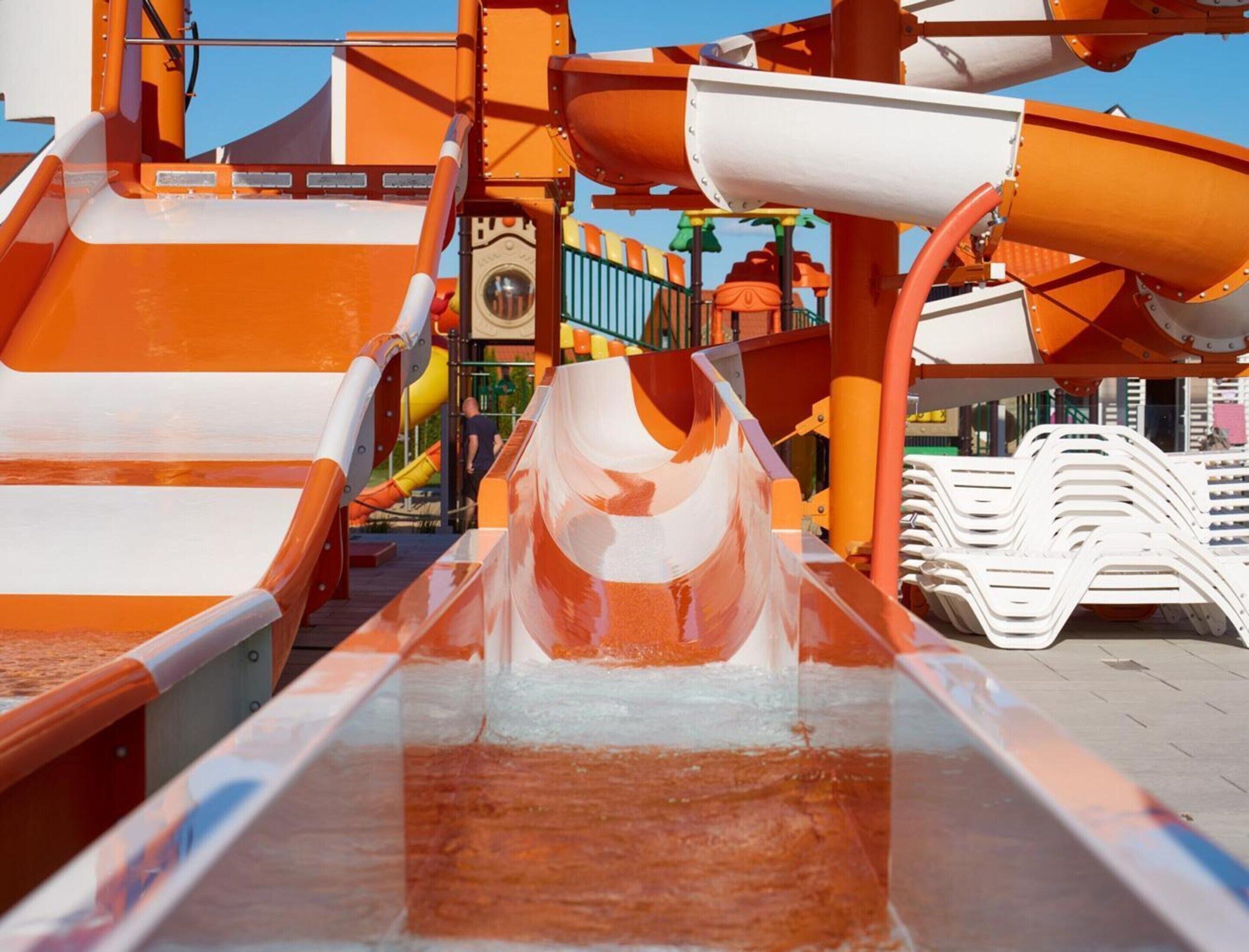 A water slide with a transparent tube leading to a pool, surrounded by orange and white structures.