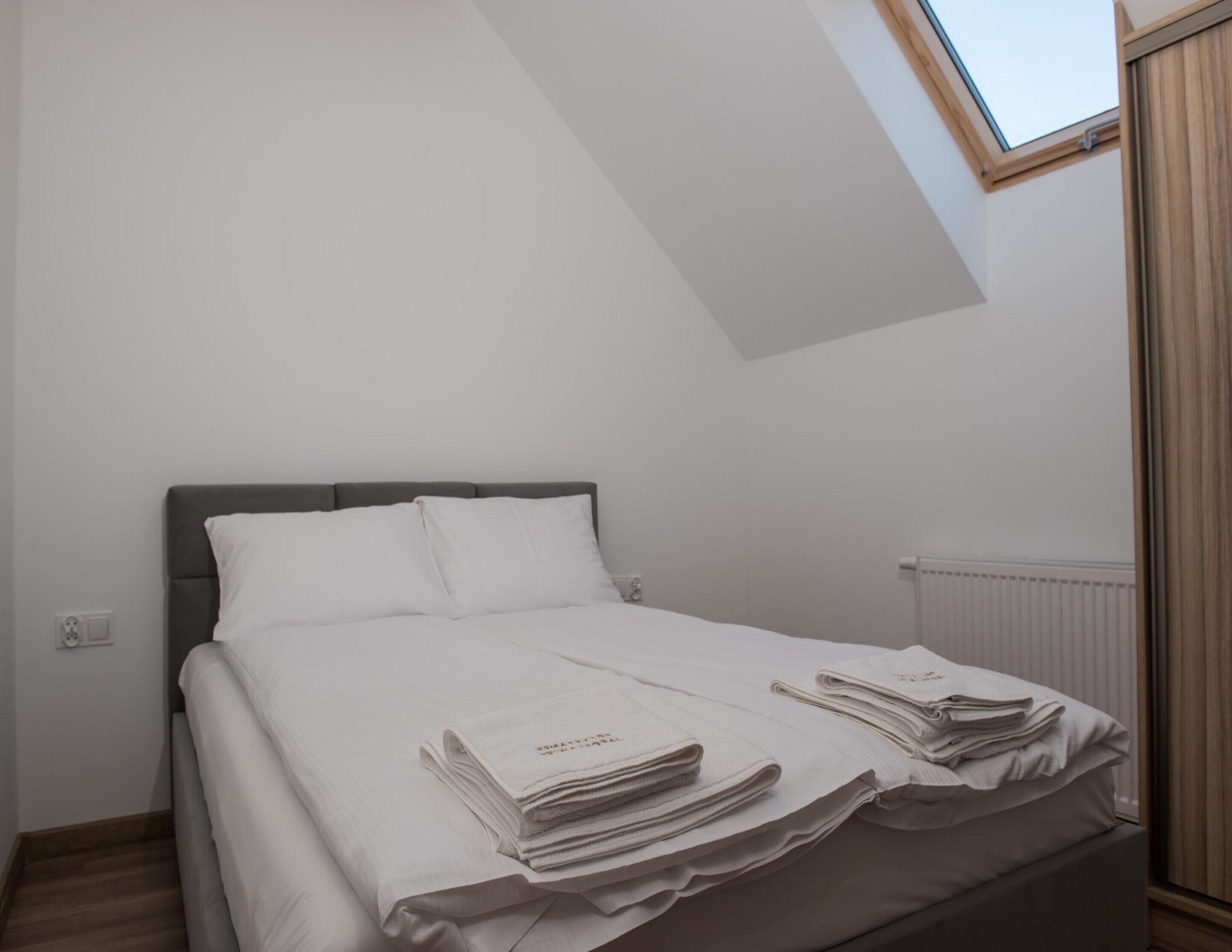 A bedroom with a bed, white linens, a skylight, and a radiator.