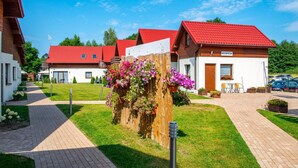 A row of wooden houses with red roofs, a wooden fence with hanging flower baskets, and a paved walkway. - 3-room Apartment on the Ground Floor, Summer Pool (Postomino)