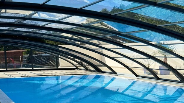 An indoor swimming pool with a glass ceiling, clear blue water, and a tiled deck. - 3-room Apartment on the Ground Floor, Summer Pool (Postomino)
