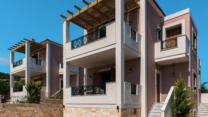 A modern multi-story residential building with balconies, a swimming pool, and stone walls. - Holiday Villa With hot tub in Adele (Rethymno)