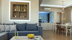 A modern living room with a grey sofa, a wooden coffee table, and a dining area with white chairs. - Holiday Villa With hot tub in Adele (Rethymno)